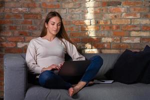 vrouw Aan bankstel met een laptop en notitieboekje foto