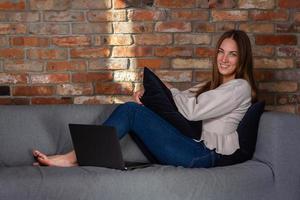 glimlachen vrouw Aan een bankstel met een laptop in voorkant van haar op zoek in camera foto