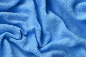 de deken van harig blauw fleece kleding stof. een achtergrond van licht blauw zacht pluche fleece materiaal met een veel van Verlichting vouwen foto