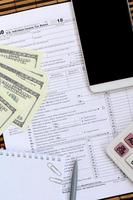 samenstelling van items aan het liegen Aan de 1040 belasting het formulier. dollar rekeningen, pen, rekenmachine, smartphone, papier klem en kladblok. de tijd naar betalen belastingen foto