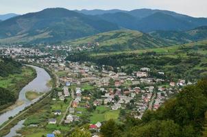 een mooi visie van de dorp van mezhgorye, Karpaten regio. een veel van woon- gebouwen omringd door hoog Woud bergen en lang rivier- foto