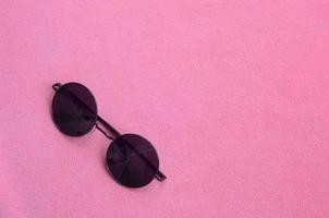 elegant zwart zonnebril met ronde bril leugens Aan een deken gemaakt van zacht en pluizig licht roze fleece kleding stof. modieus achtergrond afbeelding in vrouw kleuren foto