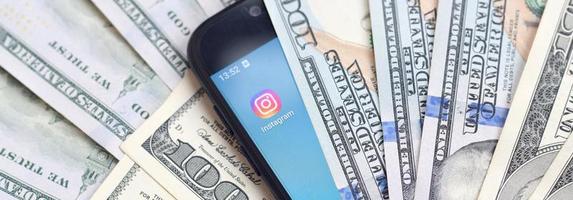 Charkov, Oekraïne - mei 3, 2021 smartphone scherm met instagram app en veel van honderd dollar rekeningen. bedrijf en sociaal netwerken concept foto