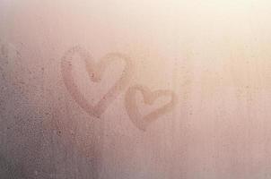 paar van abstract wazig liefde hart symbool getrokken door hand- Aan de nat venster glas met zonlicht achtergrond. sjabloon voor Valentijn dag ansichtkaarten foto