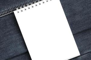 wit notitieboekje met schoon Pagina's aan het liegen Aan donker blauw jeans achtergrond. beeld met kopiëren ruimte foto