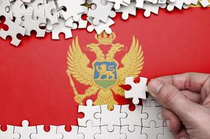 Montenegro vlag is afgebeeld Aan een tafel Aan welke de menselijk hand- vouwen een puzzel van wit kleur foto