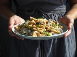 vrouw hand- houden een schotel van eigengemaakt pasta met champignons paddestoel en Carbonara saus. foto