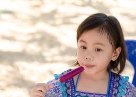 portret van mooi 4 jaren oud schattig baby Aziatisch meisje, weinig kleuter kind met mooi helder ogen eten ijs room in de park buitenshuis met kopiëren ruimte. foto