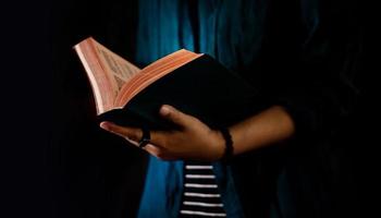 lezing concept. persoon Holding geopend Bijbel boek Aan hand. donker toon, bijgesneden beeld foto