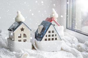 gezellig huis is gewikkeld in een muts en sjaal in een sneeuwstorm - vensterbank decor. winter, sneeuw - woningisolatie, bescherming tegen kou en slecht weer, kamerverwarmingssysteem. feestelijke stemming, kerstmis, nieuwjaar foto