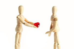 twee houten figuren van een pop, geven een rood hart, geïsoleerd Aan een wit achtergrond - afbeeldingen van de thema concepten liefde en Valentijnsdag dag. foto