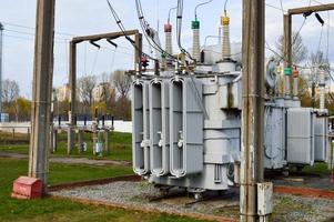 groot industrieel ijzer metaal transformator onderstation met transformatoren en hoog voltage elektrisch uitrusting en draden met piek afleiders naar levering de stad met elektriciteit foto