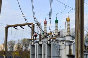 groot industrieel ijzer metaal transformator onderstation met transformatoren en hoog voltage elektrisch uitrusting en draden met piek afleiders naar levering de stad met elektriciteit foto