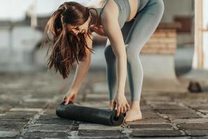 vrouw rollend omhoog yoga mat en voorbereidingen treffen naar buitenshuis opleiding foto