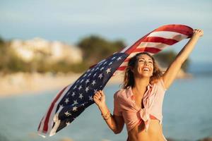 vrouw met ons nationaal vlag genieten van dag Aan een strand foto