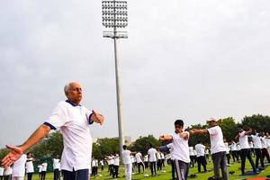 nieuw Delhi, Indië, juni 21 2022 - groep yoga oefening sessie voor mensen Bij Yamuna sport- complex in Delhi Aan Internationale yoga dag, groot groep van volwassenen Bijwonen yoga klasse in krekel stadion foto