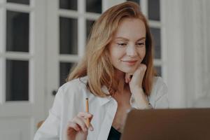 nadenkend vrouw werknemer denken over- idee, werken Aan project Bij laptop, Holding potlood. afgelegen baan foto