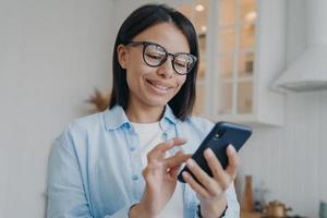 mobiel apps. glimlachen vrouw in bril Holding smartphone, winkelen, gebruik makend van online Diensten Bij huis foto