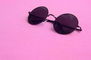 elegant zwart zonnebril met ronde bril leugens Aan een deken gemaakt van zacht en pluizig licht roze fleece kleding stof. modieus achtergrond afbeelding in vrouw kleuren foto