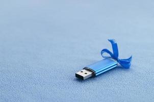 briljant blauw USB flash geheugen kaart met een blauw boog leugens Aan een deken van zacht en harig licht blauw fleece kleding stof. klassiek vrouw geschenk ontwerp voor een geheugen kaart foto