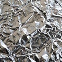 dun gerimpeld vel van verpletterd blik aluminium zilver folie achtergrond met glimmend verfrommeld oppervlakte voor structuur foto