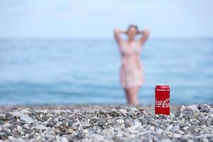 antalya, kalkoen - mei 18, 2021 origineel coca cola rood blik kan leugens Aan klein ronde kiezelsteen stenen dichtbij naar zee oever. Coca Cola kan en vrouw Aan strand foto