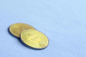 twee gouden bitcoins leugens Aan een deken gemaakt van zacht en pluizig licht blauw fleece kleding stof. fysiek visualisatie van virtueel crypto valuta foto