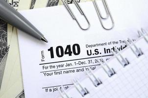 de pen, notitieboekje en dollar rekeningen is leugens Aan de belasting het formulier 1040 ons individu inkomen belasting opbrengst. de tijd naar betalen belastingen foto