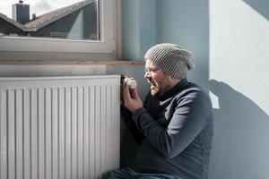 geërgerd Mens in warm kleren bochten de radiator thermostaat naar minimum. concept van crisis en toenemen in brandstof kosten. voorbereidingen treffen voor een verkoudheid winter. foto