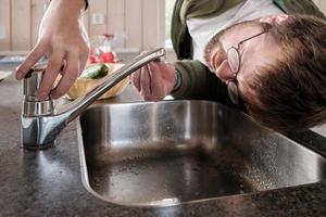 Mens looks in verbijstering Bij de kraan van welke water heeft gestopt stromend, bovenstaand de wasbak, in de keuken. foto