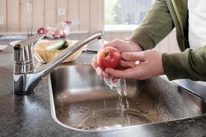 mannetje handen wassen een rijp appel onder rennen water, in de wasbak, in de keuken. foto