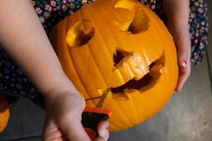 halloween voorbereiding. kind snijwerk pompoen in jack-o-lantern terwijl zittend Aan de verdieping in de huis. foto