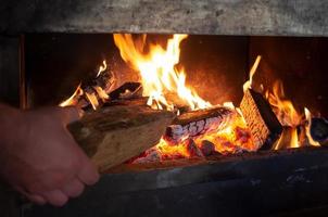 hand- zet een log Aan een brand naar warmte een huis foto