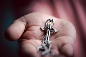 geestelijk christen hand- Holding Jezus kruis ketting in de palm met geloof en geloven. foto