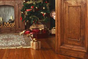 kind jongen gluurt uit van de deur met een Kerstmis geschenk doos foto