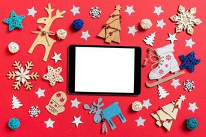 top visie van digitaal tablet, vakantie speelgoed en decoraties Aan rood Kerstmis achtergrond. nieuw jaar tijd concept foto