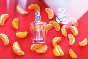 parfum fles voor Dames Aan een rood achtergrond, versierd met mandarijn- plakjes. de concept van een vers citrus parfum foto