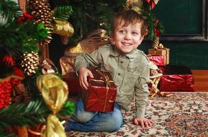 kind jongen zittend onder de Kerstmis boom met geschenk doos foto