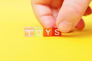woord speelgoed met kleurrijk kubussen van kralen en kind hand- Aan geel achtergrond foto