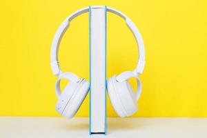 audio boek concept met modern wit hoofdtelefoons en hardcover boek Aan een geel achtergrond. luisteren naar een boek. foto