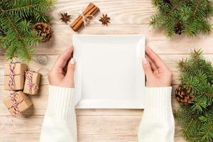 vrouw hand- houden top visie. wit plein bord Aan een houten tafel met Kerstmis decoratie. nieuw jaar concept foto