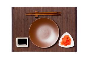 leeg ronde bruin bord met eetstokjes voor sushi, gember en soja saus Aan donker bamboe mat achtergrond. top visie met kopiëren ruimte voor u ontwerp foto