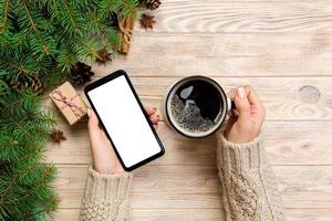 vrouw handen Holding modern smartphone met moskee omhoog en mok van koffie Aan houten tafel met Kerstmis decoratie. top visie foto