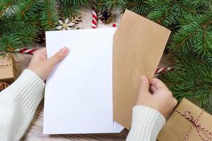 handen met notitieboekje en een omhullen voor brief. een meisje is klaar naar sturen een brief met wensen naar de kerstman claus foto
