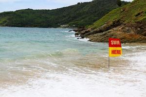 rood met geel zwemmen horen vlag Aan de strand en zee naar vertellen of informeren reiziger , toerist en mensen kan zwemmen in deze Oppervlakte Bij phuket, Thailand. zeegezicht met Golf, lucht en berg achtergrond. foto