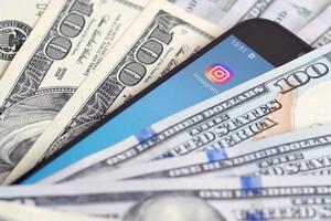 Charkov, Oekraïne - mei 12, 2022 smartphone scherm met instagram app en veel van honderd dollar rekeningen. bedrijf en sociaal netwerken concept foto