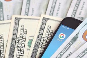 Charkov, Oekraïne - mei 12, 2022 smartphone scherm met google app en veel van honderd dollar rekeningen. bedrijf en sociaal netwerken concept foto