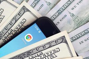 Charkov, Oekraïne - mei 12, 2022 smartphone scherm met google chroom app en veel van honderd dollar rekeningen. bedrijf en sociaal netwerken concept foto