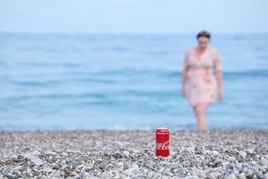 Charkov, Oekraïne - mei 12, 2022 origineel coca cola rood blik kan leugens Aan klein ronde kiezelsteen stenen dichtbij naar zee oever. Coca Cola kan en vrouw Aan strand foto