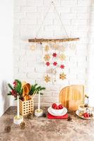 een boeket van net takken, brandend kaarsen, rood ballen en een handgemaakt slinger Aan een wit steen muur in de interieur van een modern keuken . foto